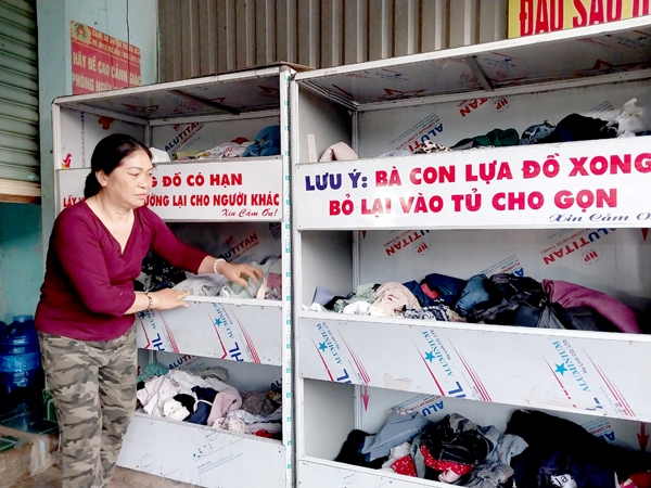 Bà Ngô Thị Lâm sắp xếp lại những bộ áo quần cũ đặt phía trước nhà để ai cần thì lấy